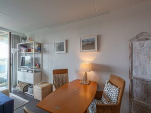 A hotel room with a dining table, wicker chairs, a lamp, a bookshelf, and two framed pictures on the wall. - Apartment With Kitchen (Callantsoog)
