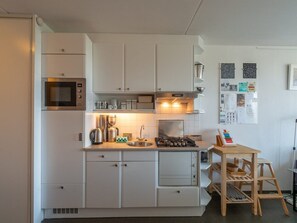 A compact kitchen with white cabinets, a built-in microwave, a gas stove, and a coffee maker. - Apartment With Kitchen (Callantsoog)