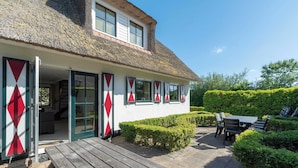A traditional house with a thatched roof, a wooden deck, and a garden with neatly trimmed bushes.
