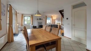 A spacious dining area with a large wooden table and chairs, a kitchen in the background, and a staircase leading to another level.