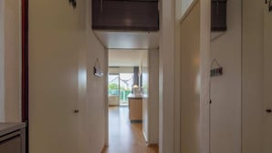 Un corridoio stretto con pavimento in legno che conduce a una zona cucina con finestra e vista all'esterno.