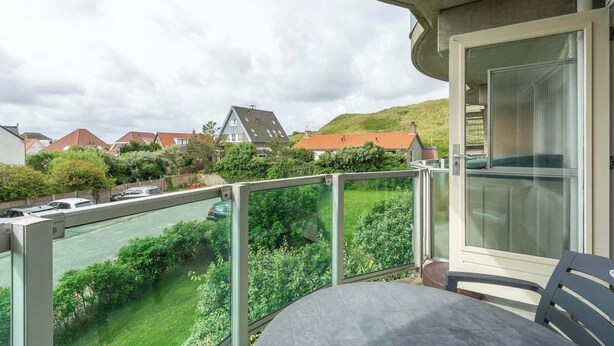 Un balcone con tavolo e sedie, affaccia su un paesaggio verde e case.