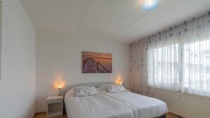 Una camera da letto con un letto, comodini, un quadro e una finestra con tende.