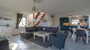 A spacious living room with a modern staircase, a dining area, and a kitchen with blue cabinets. - Villa in Callantsoog Near Beach & Sea (Callantsoog)