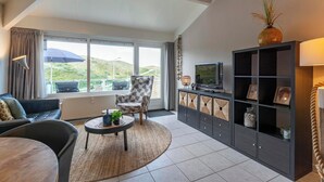 A modern living room with a sofa, armchair, and coffee table, a television, and a bookshelf. - Apartment in Callantsoog by the Beach (Callantsoog)
