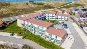 A coastal residential area with a multi-story building featuring balconies, a parking lot, and a road leading to the beach. - Apartment in Callantsoog by the Beach (Callantsoog)