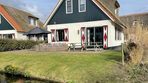 A traditional house with a steep gabled roof, a small porch with a bench, and a grassy yard with a pond. - Villa in Callantsoog With Whirlpool and Beach (Callantsoog)