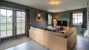 A modern living room with a sectional sofa, a TV, and a dining table. - Villa in Callantsoog With Whirlpool and Beach (Callantsoog)