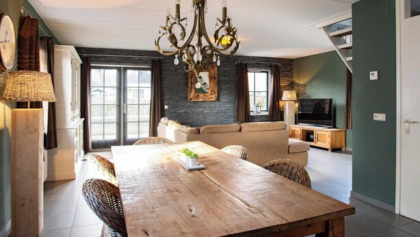 A dining area with a wooden table, wicker chairs, a chandelier, and a television in the background. - Villa in Callantsoog With Whirlpool and Beach (Callantsoog)