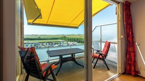 Un balcon avec une table et des chaises, un parasol jaune et une vue sur un parking et le paysage environnant.