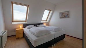 Une chambre à coucher avec un lit, deux tables de chevet, un radiateur et deux fenêtres de toit.