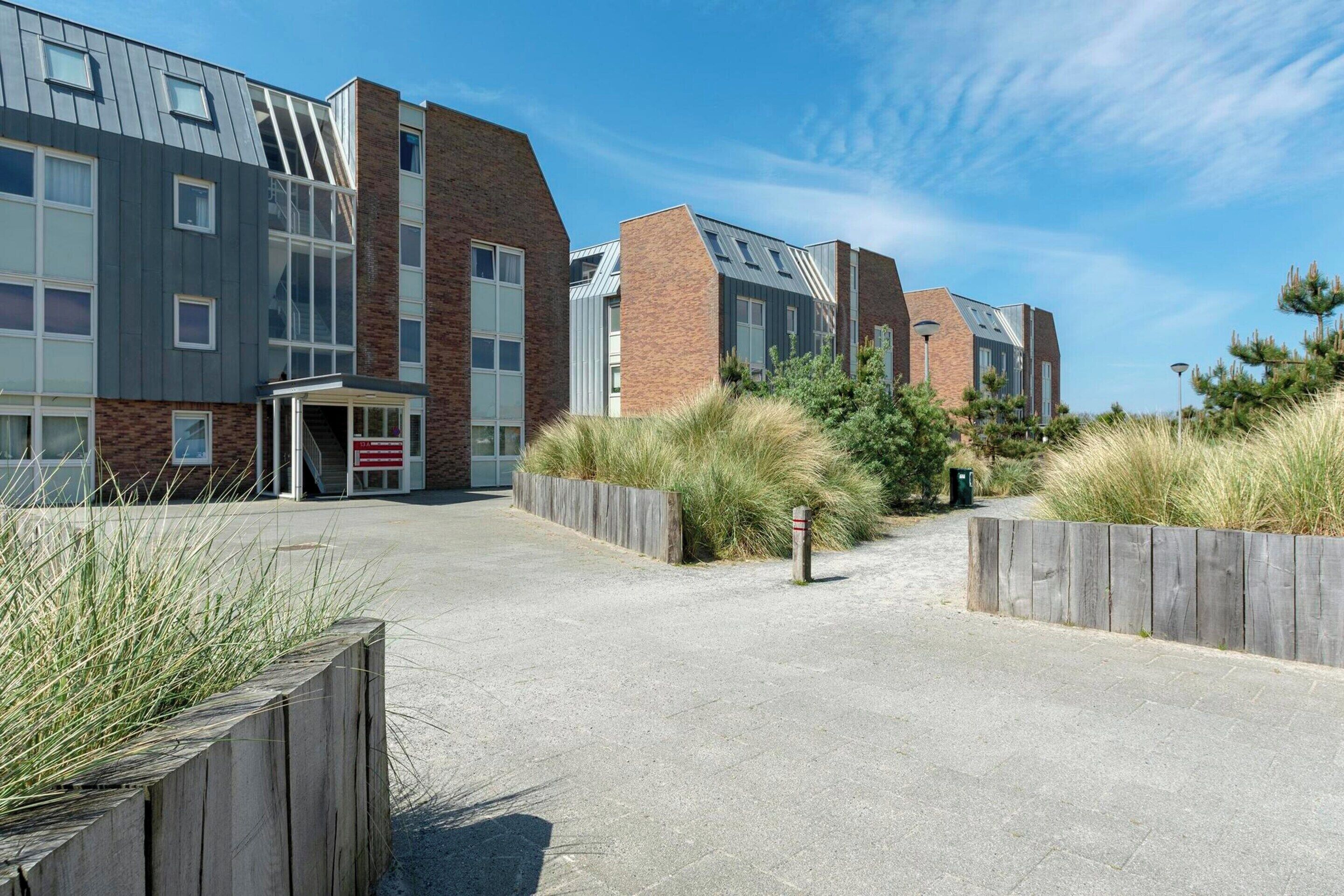 A modern building with a mix of brick and metal exterior, a paved entrance, and surrounding grassy areas.
