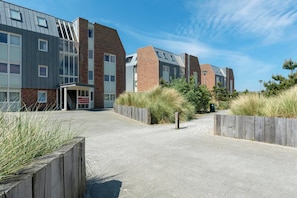 A modern building with a mix of brick and metal exterior, a paved entrance, and surrounding grassy areas. - Elegant Penthouse With Patio (Callantsoog)