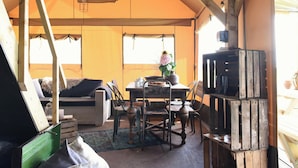 A tented accommodation with a dining area, a sofa, and a rustic wooden shelf. - Beach Lodge Callantsoog Near the Sea (Callantsoog)