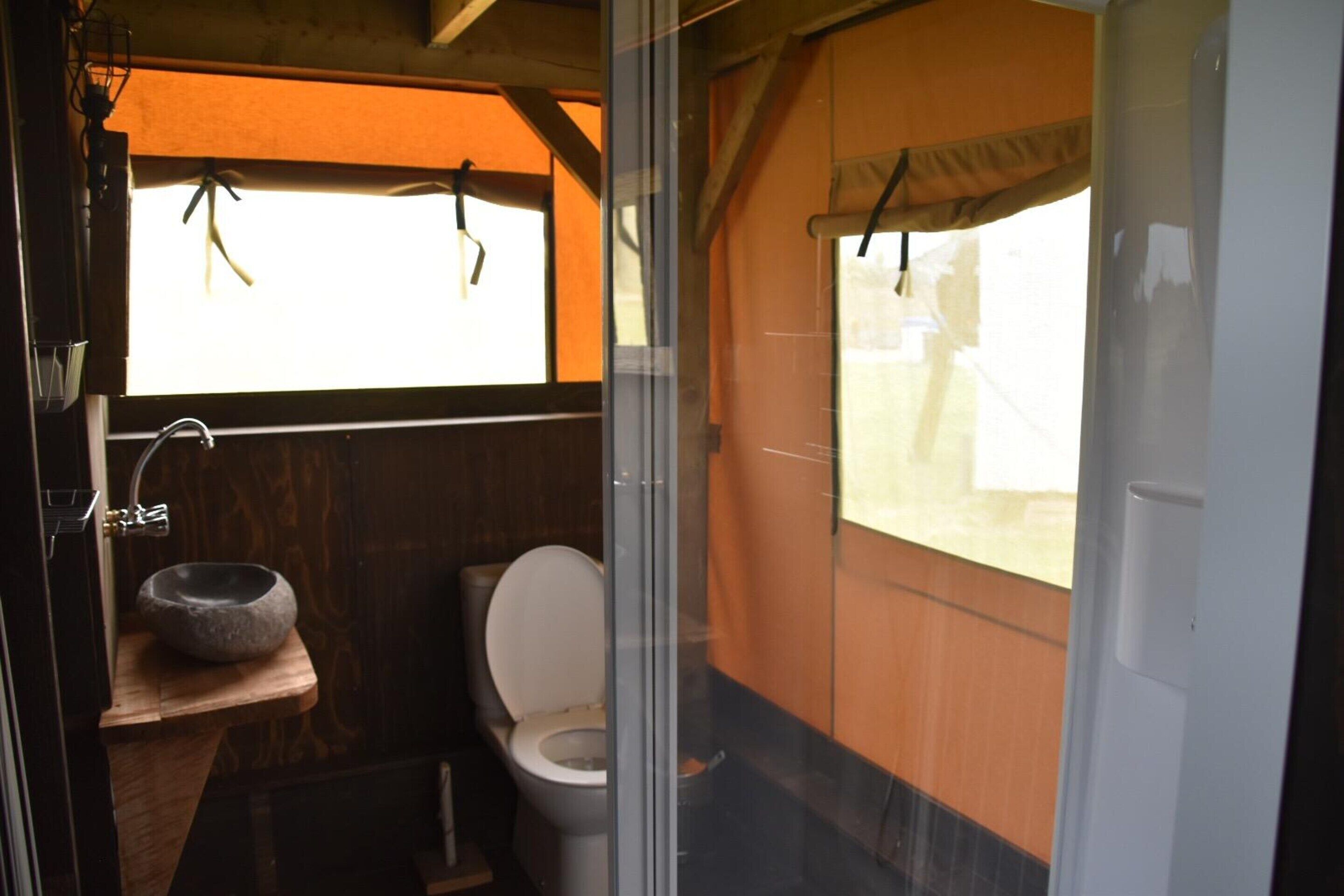 A compact bathroom with a stone sink, a toilet, and a window with a curtain.