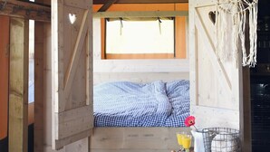 A cozy wooden cabin with a bed, a small table with breakfast items, and a macrame decoration. - Beach Lodge Callantsoog Near the Sea (Callantsoog)
