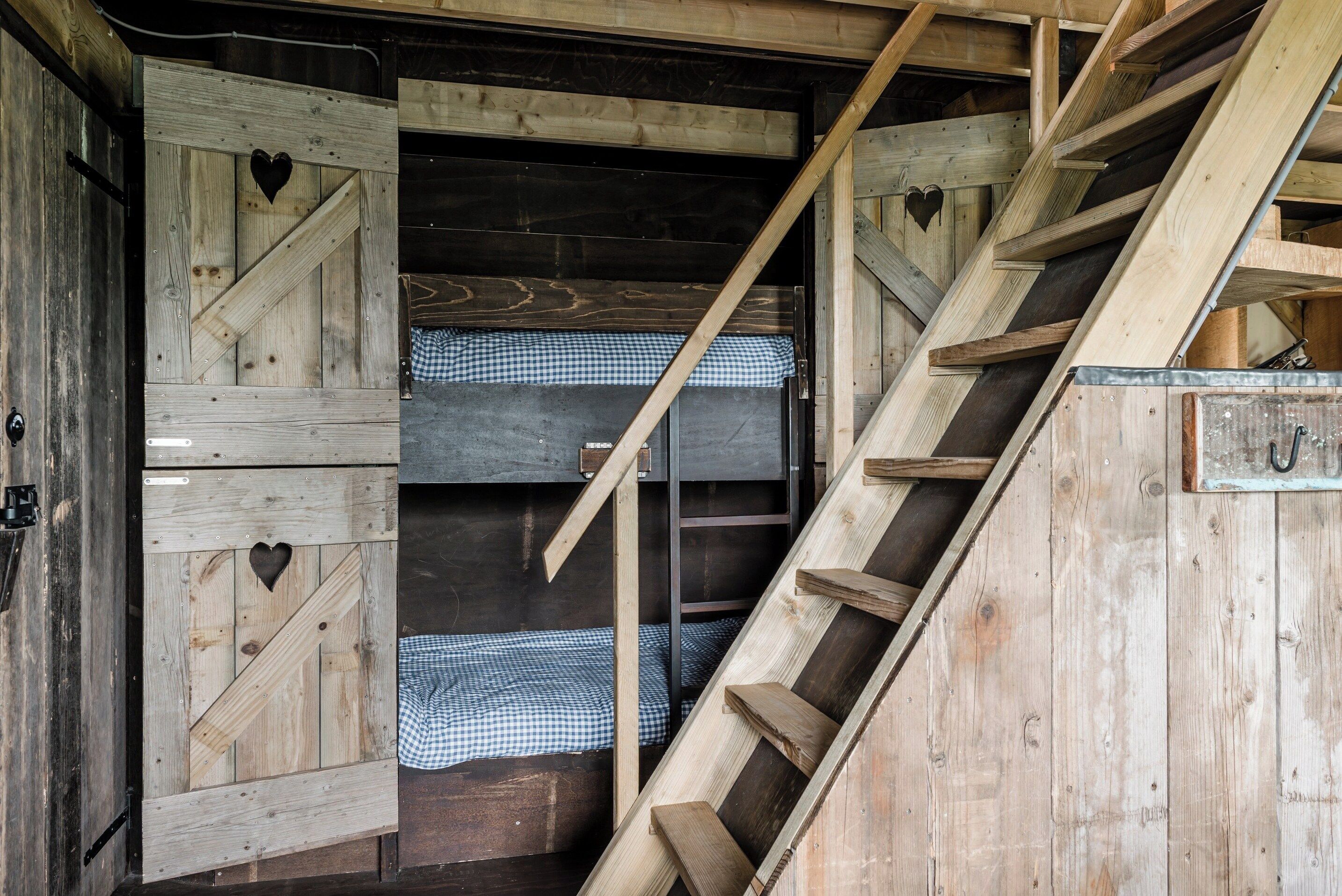 A rustic wooden staircase leading to a lofted sleeping area with checkered bedding.