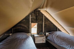 A small, enclosed sleeping area with two beds, a wooden crate, and a view of the outside through a window.