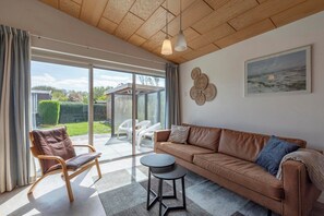 Een moderne woonkamer met een bruine leren bank, een houten stoel, een klein rond tafeltje en een grote schuifdeur die uitkomt op een patio.