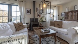 Un salon chaleureux avec une cheminée, des canapés blancs, une table basse et un luminaire suspendu.