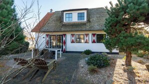 A traditional house with a thatched roof, a small porch, and a garden with a pine tree and rocks. - Dutch Beach Hideaway w/ Parking (Callantsoog)