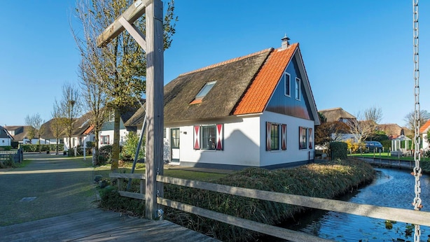 A house with a thatched roof, white walls, and a wooden dock extending over a canal. - Dutch Beach Hideaway w/ Parking (Callantsoog)