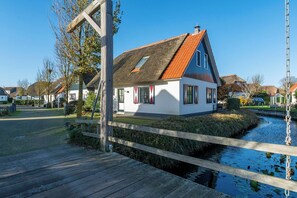 A house with a thatched roof, white walls, and a wooden dock extending over a canal. - Dutch Beach Hideaway w/ Parking (Callantsoog)