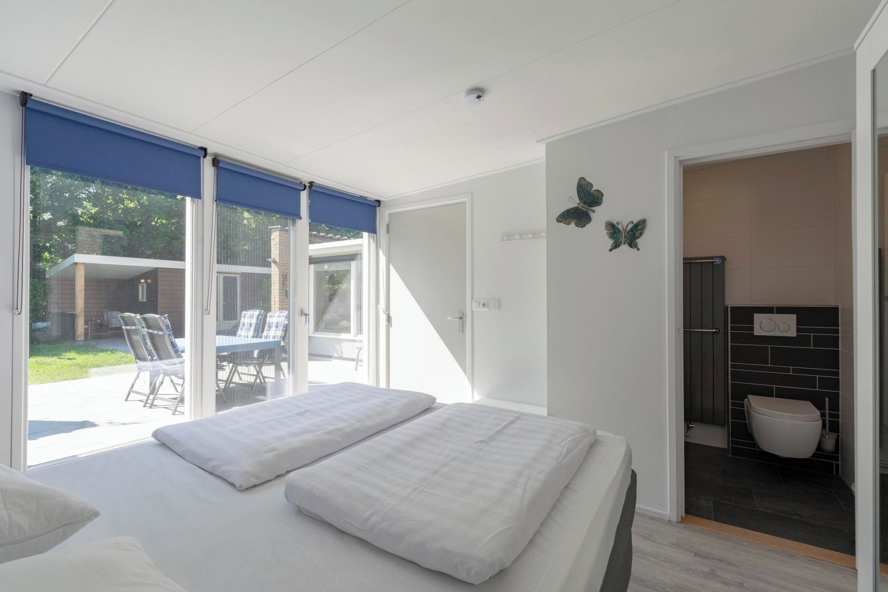 Un dormitorio con una cama grande, un ventanal corredero que da a un patio, y un baño visible a través del ventanal.
