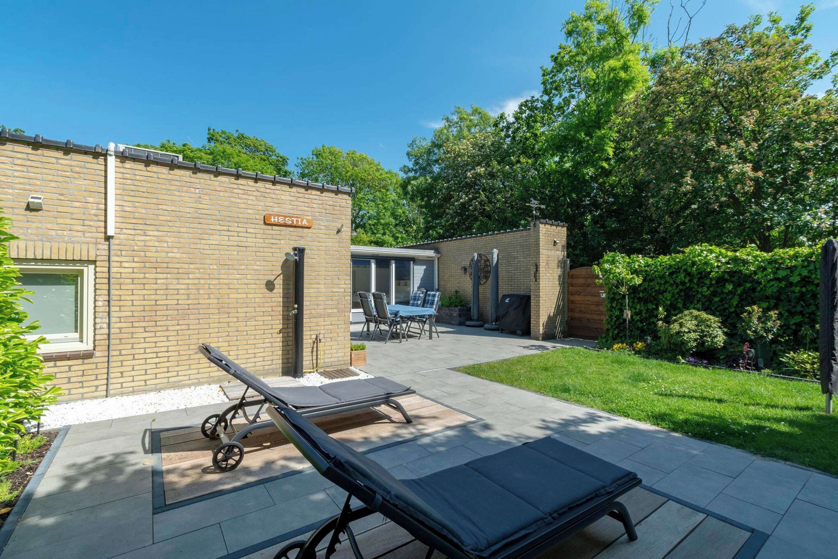 A hotel with a brick exterior, a patio area with sun loungers, a table and chairs, and a well-maintained garden.