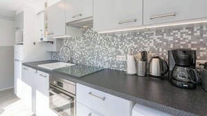 A modern kitchen with white cabinets, a glass countertop, a tiled backsplash, and a coffee maker. - Bungalow in Sint Maartenszee Near Beach (Sint Maartensvlotbrug)