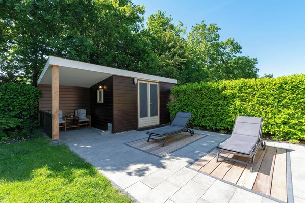 Un patio extérieur moderne doté d’un espace salon couvert, d’un fauteuil et d’une petite table.
