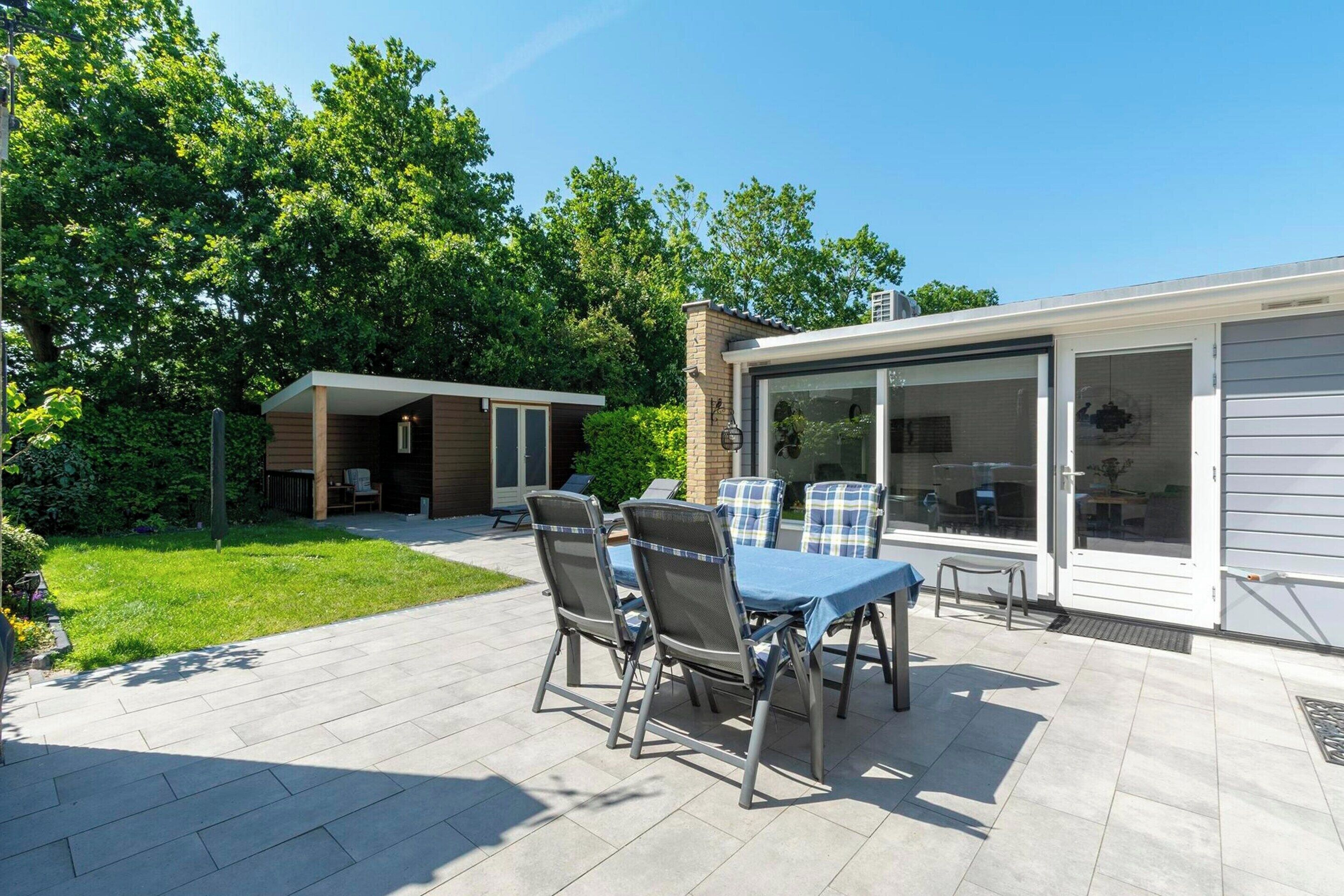 An outdoor patio with a table and chairs, a covered seating area, and a building with large windows and a garage door.