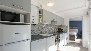 A compact kitchen with a Liebherr refrigerator, a microwave, a sink, and a washing machine. - Bungalow in Sint Maartenszee Near Beach (Sint Maartensvlotbrug)
