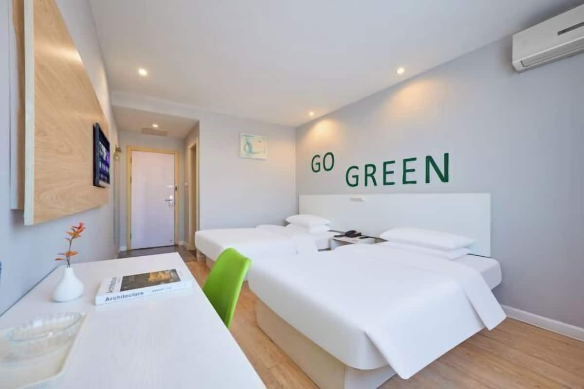 Habitación de hotel con dos camas, un escritorio, una silla, televisor montado en la pared y un cartel que dice 'GO GREEN'.