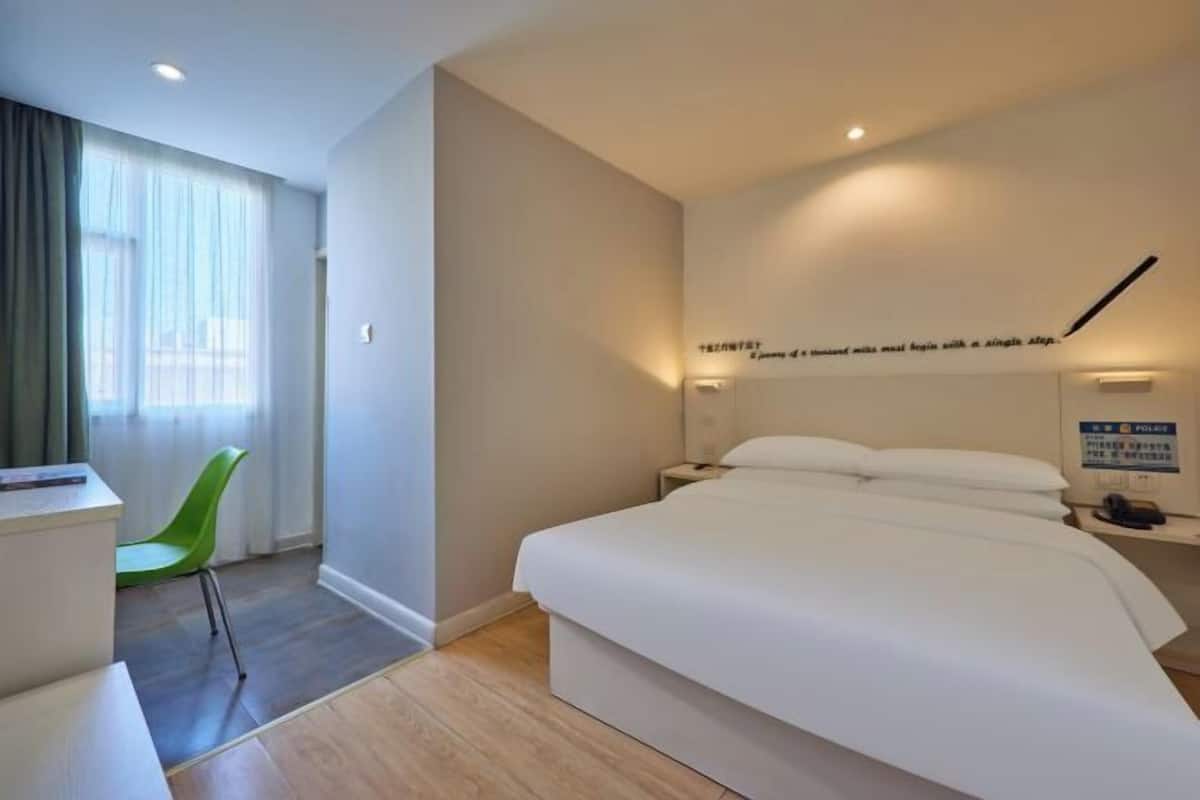 Habitación de hotel con cama, escritorio, silla, mesita de noche y ventana con cortinas.