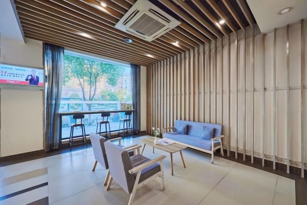 A modern hotel lobby with a seating area, a television screen, and a large window.