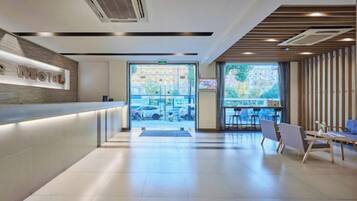 A modern hotel lobby with a reception desk, seating area, and large windows.
