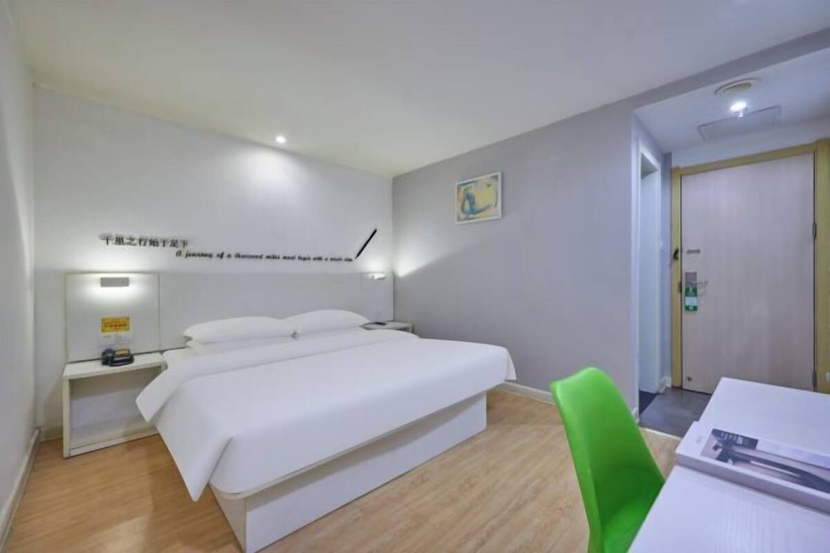Una habitación de hotel con cama, mesita de noche, silla y puerta que da a un baño.