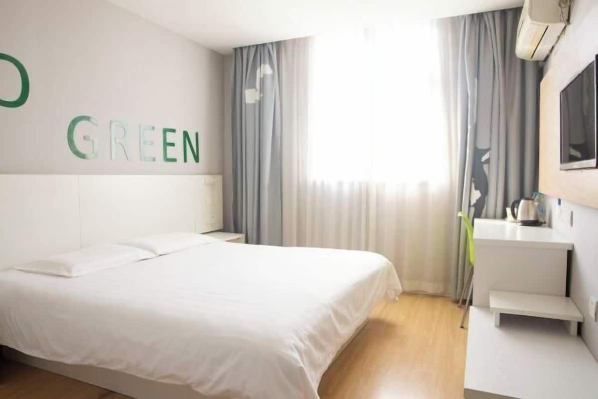 Una habitación de hotel moderna con una cama grande, una mesita de noche, un escritorio pequeño, un espejo y una ventana con cortinas.