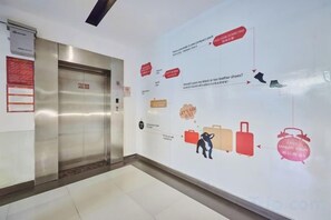 Um elevador com visor digital, parede com mural de tema de viagem e chão ladrilhado.