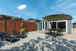 Un espace patio avec une table et des chaises, un grand parasol et un mur en briques.