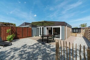 Un jardin avec un espace patio, une table et des chaises, un parasol vert et une clôture en bois.