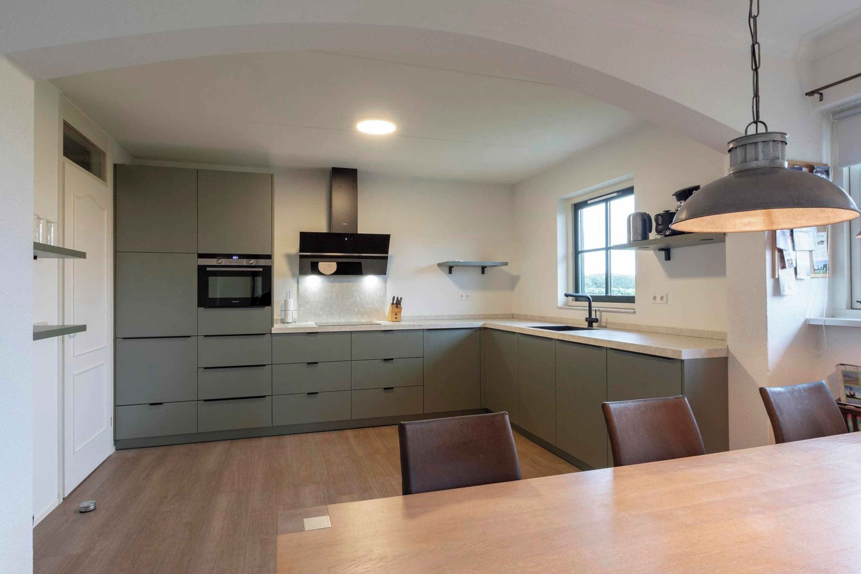 Una cucina moderna con mobili grigi, forno integrato e zona pranzo con tavolo e sedie in legno.