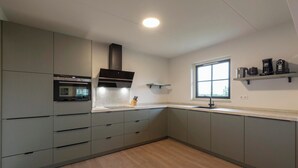 A modern kitchen with grey cabinets, a built-in oven, a range hood, and a window with a view. - Villa in Callantsoog Near Beach and Dunes (Callantsoog)