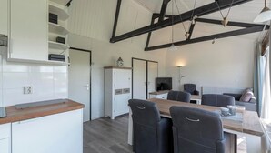 A modern kitchen with white cabinetry, a wooden countertop, and a dining area with a table and chairs. - Boerenslag-2 Bungalow, 5-guests Opposite Beach (Sint Maartensvlotbrug)
