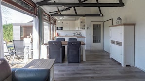 A spacious kitchen with white cabinets, a dining area with a table and chairs, and a large window providing natural light. - Boerenslag-2 Bungalow, 5-guests Opposite Beach (Sint Maartensvlotbrug)