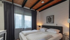 A bedroom with two beds, a desk, and a window with curtains. - Boerenslag-2 Bungalow, 5-guests Opposite Beach (Sint Maartensvlotbrug)