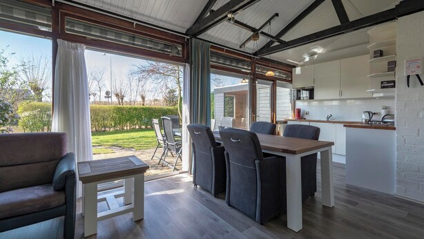 A modern kitchen with white cabinets, a wooden countertop, and a dining area with a table and chairs. - Boerenslag-2 Bungalow, 5-guests Opposite Beach (Sint Maartensvlotbrug)