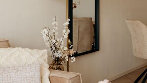 A room with a beige sofa, a white textured pillow, a vase with white flowers, a mirror, and a chair. - Comfortable 2-guest De Vlijt First Class Suite (De Cocksdorp)