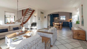 A spacious living area with a sofa, wicker chairs, a dining table, and a kitchen in the background. - De Buitenplaats 7 Villa With Dune Views (Callantsoog)